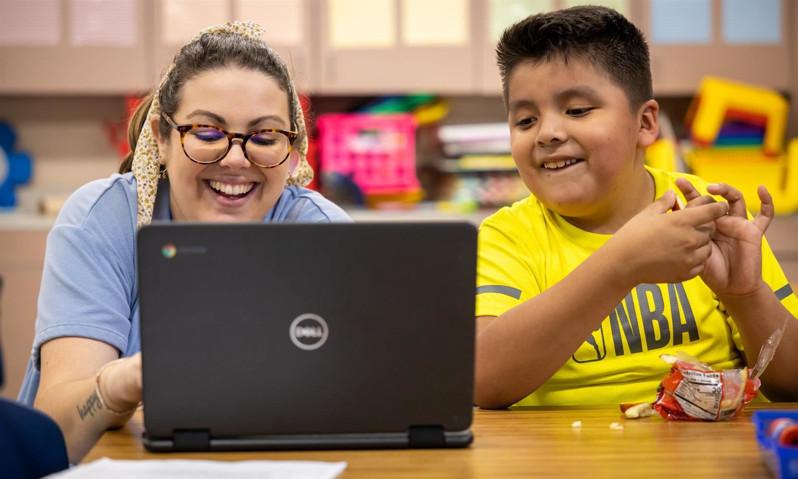 A teacher a student smile while working on a laptop